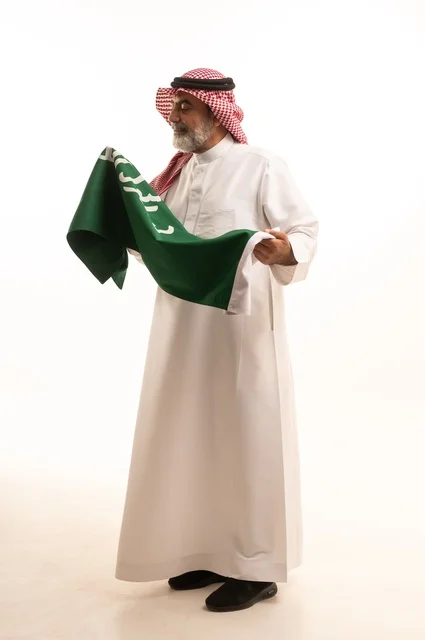 إيماءات الفخر و السرور بالانتماء للوطن, إحياء ذكرى اليوم الوطني السعودي 23 سبتمبر, بورتريه لرجل عربي خليجي سعودي مبتسم يرتدي الشماغ و الثوب التقليدي يحمل بيده علم يوم التأسيس، يوم بدينا 1727 م، الجسم بالطول الكامل، خلفية بيضاء