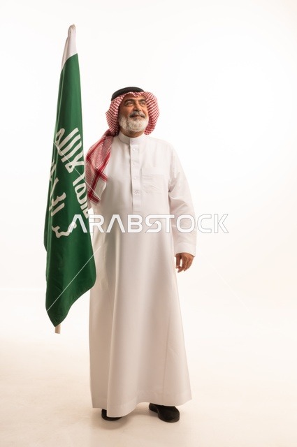 إحياء ذكرى اليوم الوطني السعودي 23 سبتمبر, إيماءات الفخر و السرور بالانتماء للوطن, بورتريه لرجل عربي خليجي سعودي مبتسم يرتدي الشماغ و الثوب التقليدي يحمل بيده علم يوم التأسيس، يوم بدينا 1727 م، الجسم بالطول الكامل، خلفية بيضاء