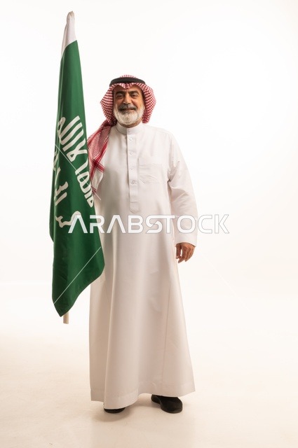 إحياء ذكرى اليوم الوطني السعودي 23 سبتمبر, إيماءات الفخر و السرور بالانتماء للوطن, بورتريه لرجل عربي خليجي سعودي مبتسم يرتدي الشماغ و الثوب التقليدي يحمل بيده علم يوم التأسيس، يوم بدينا 1727 م، الجسم بالطول الكامل، خلفية بيضاء