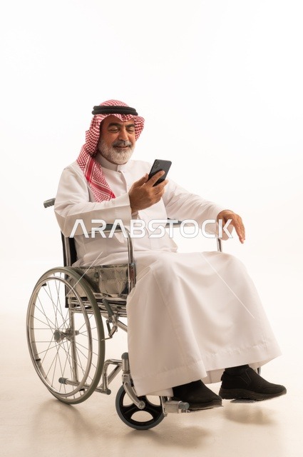 Communicating with family and friends, providing devices and equipment that help with movement and mobility, caring for people with disabilities and providing for their special needs, a portrait of a Saudi Arabian Gulf man with special needs wearing traditional thobe and shemagh sitting in a wheelchair and holding a mobile phone, white background
