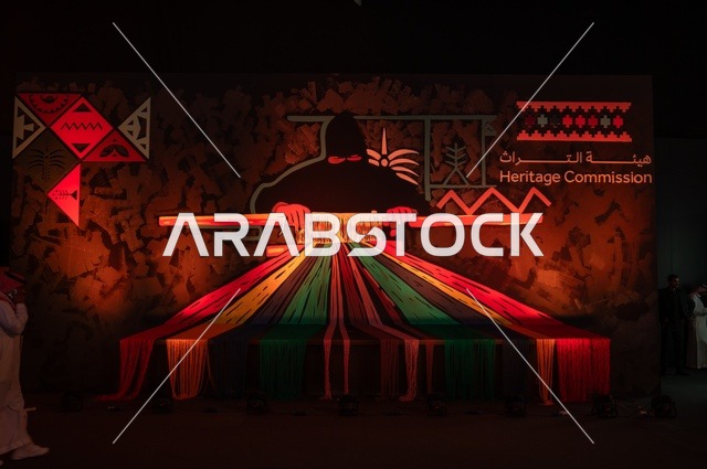 هيئة التراث هيئة عربية سعودية أنشئت عام ٢٠٢٠ كجزء من وزارة الثقافة، هدفها حماية التراث الثقافي للمملكة العربية السعودية والحفاظ عليه وتنميته، بوستر في معرض لإمرأة خليجية عربية سعودية تنسج الخيوط الملونة