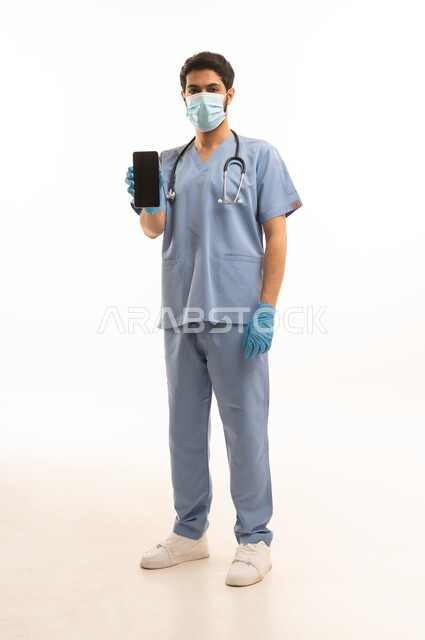 عرض شاشة سوداء فارغة عبر الهاتف المحمول، مفهوم الطب والرعاية الصحية، بورتريه لممرص عربي خليجي سعودي يرتدي اليونيفورم مع السماعة الطبية يقدم الخدمات الصحية للمرضى، مهنة ووظيفة طبية، العمل في القطاع الصحي في المملكة، الجسم بالطول الكامل، خلفيه بيضاء