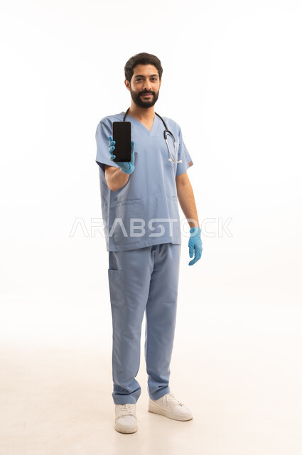 عرض شاشة سوداء فارغة عبر الهاتف المحمول، مفهوم الطب والرعاية الصحية، بورتريه لممرص عربي خليجي سعودي يرتدي اليونيفورم مع السماعة الطبية يقدم الخدمات الصحية للمرضى، مهنة ووظيفة طبية، العمل في القطاع الصحي في المملكة، الجسم بالطول الكامل، خلفيه بيضاء