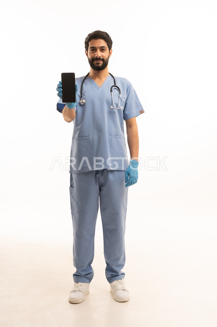 عرض شاشة سوداء فارغة عبر الهاتف المحمول، مفهوم الطب والرعاية الصحية، بورتريه لممرص عربي خليجي سعودي يرتدي اليونيفورم مع السماعة الطبية يقدم الخدمات الصحية للمرضى، مهنة ووظيفة طبية، العمل في القطاع الصحي في المملكة، الجسم بالطول الكامل، خلفيه بيضاء