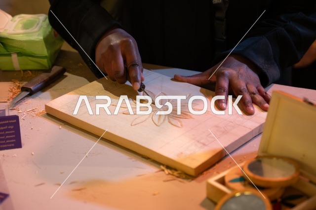 رجل ينقش على إطار خشبي لتبدو قطعة فنية يدوية، تزيين الإطار، استخدام معدات النقش، ايدي ذات بشرة سوداء، تراث العمل الفني اليدوي، أعمال تراثية نقش رسومات زهور