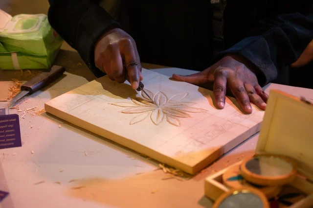 A man is carving on a wooden frame to make it look like a handmade piece of art, decorating the frame, using carving tools, hands with black skin, the heritage of handmade art, traditional works carving flower designs.