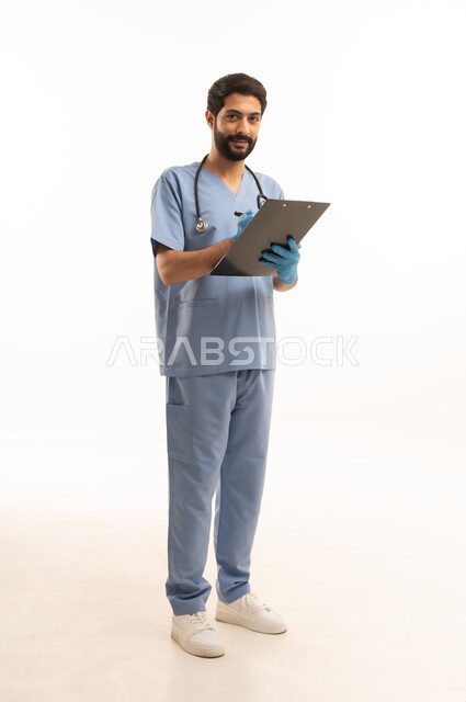 تسجيل وتدوين المعلومات، مفهوم الطب والرعاية الصحية، بورتريه لممرض عربي خليجي سعودي يرتدي اليونيفورم مع السماعة الطبية يقدم الخدمات الصحية للمرضى في المراكز والمستشفيات، مهنة ووظيفة طبية، العمل في القطاع الصحي في المملكة، الجسم بالطول الكامل، خلفيه بيضاء