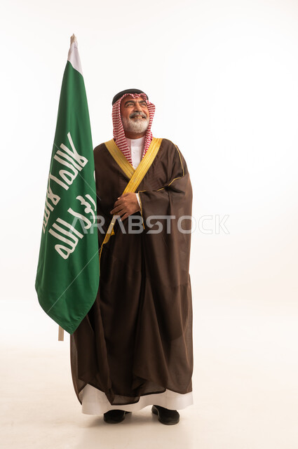 الاحتفال بذكرى اليوم الوطني السعودي 23 سبتمبر, إيماءات الفخر و السرور بالانتماء للوطن, بورتريه لرجل عربي خليجي سعودي مبتسم يرتدي الشماغ و الثوب التقليدي مع البشت يحمل بيده علم يوم التأسيس، يوم بدينا 1727 م، الجسم بالطول الكامل، خلفية بيضاء