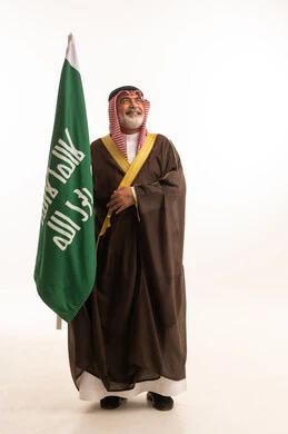 الاحتفال بذكرى اليوم الوطني السعودي 23 سبتمبر, إيماءات الفخر و السرور بالانتماء للوطن, بورتريه لرجل عربي خليجي سعودي مبتسم يرتدي الشماغ و الثوب التقليدي مع البشت يحمل بيده علم يوم التأسيس، يوم بدينا 1727 م، الجسم بالطول الكامل، خلفية بيضاء