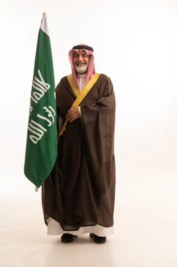 الاحتفال بذكرى اليوم الوطني السعودي 23 سبتمبر, إيماءات الفخر و السرور بالانتماء للوطن, بورتريه لرجل عربي خليجي سعودي مبتسم يرتدي الشماغ و الثوب التقليدي مع البشت يحمل بيده علم يوم التأسيس، يوم بدينا 1727 م، الجسم بالطول الكامل، خلفية بيضاء
