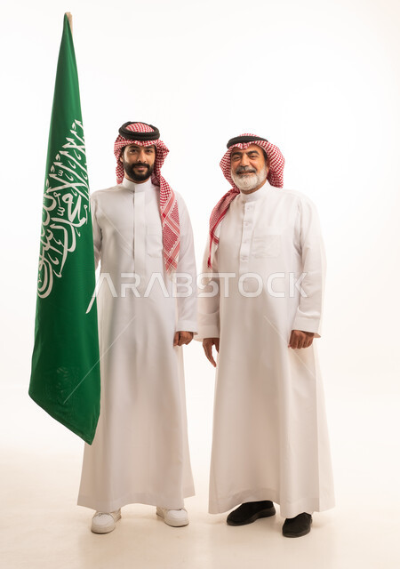  إيماءات الفخر و السرور بالانتماء للوطن, الاحتفال بذكرى اليوم الوطني السعودي 23 سبتمبر, بورتريه لرجل عربي خليجي سعودي مبتسم يرتدي الشماغ و الثوب التقليدي مع البشت يحمل بيده علم يوم التأسيس ويقف مع والده، يوم بدينا 1727 م، الجسم بالطول الكامل، خلفية بيضاء