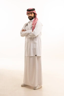 مفهوم الطب والرعاية الصحية، بورتريه لطبيب عربي خليجي سعودي يرتدي الثوب التقليدي مع المعطف والسماعة الطبية يقدم الخدمات الصحية للمرضى في المراكز والمستشفيات، مهنة ووظيفة طبية، العمل في القطاع الصحي في المملكة، الجسم بالطول الكامل، خلفيه بيضاء