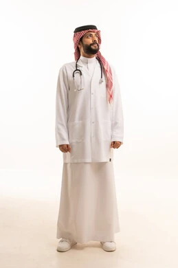 مفهوم الطب والرعاية الصحية، بورتريه لطبيب عربي خليجي سعودي يرتدي الثوب التقليدي مع المعطف والسماعة الطبية يقدم الخدمات الصحية للمرضى في المراكز والمستشفيات، مهنة ووظيفة طبية، العمل في القطاع الصحي في المملكة، الجسم بالطول الكامل، خلفيه بيضاء