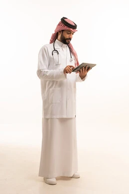 استخدام الجهاز اللوحي، مفهوم الطب والرعاية الصحية، بورتريه لطبيب عربي خليجي سعودي يرتدي الثوب التقليدي مع المعطف والسماعة يقدم الخدمات الصحية للمرضى في المراكز والمستشفيات، مهنة ووظيفة طبية، العمل في القطاع الصحي في المملكة، الجسم بالطول الكامل، خلفيه بيضاء
