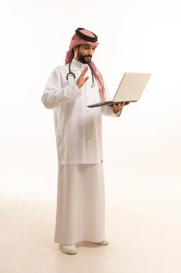 العمل عبر الحاسوب المحمول، مفهوم الطب والرعاية الصحية، بورتريه لطبيب عربي خليجي سعودي يرتدي الثوب التقليدي مع المعطف والسماعة يقدم الخدمات الصحية للمرضى في المراكز والمستشفيات، مهنة ووظيفة طبية، العمل في القطاع الصحي في المملكة، الجسم بالطول الكامل، خلفيه بيضاء