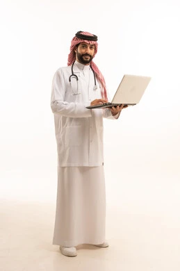 العمل عبر الحاسوب المحمول، مفهوم الطب والرعاية الصحية، بورتريه لطبيب عربي خليجي سعودي يرتدي الثوب التقليدي مع المعطف والسماعة يقدم الخدمات الصحية للمرضى في المراكز والمستشفيات، مهنة ووظيفة طبية، العمل في القطاع الصحي في المملكة، الجسم بالطول الكامل، خلفيه بيضاء