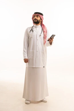 مهنة ووظيفة طبية، مفهوم الطب والرعاية الصحية، بورتريه لطبيب عربي خليجي سعودي يرتدي الثوب التقليدي مع المعطف والسماعة الطبية يحمل بيده الهاتف المحمول، تقديم الخدمات الصحية للمرضى، العمل في القطاع الصحي في المملكة، الجسم بالطول الكامل، خلفيه بيضاء