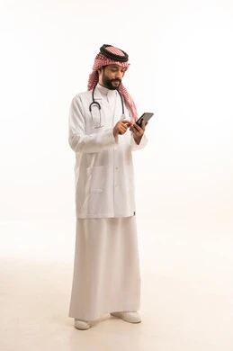 Medical profession and job, concept of medicine and healthcare, portrait of a Saudi Arabian Gulf Arab doctor wearing traditional thobe with coat and stethoscope holding a mobile phone, providing health services to patients, working in the health sector in the Kingdom, full body, white background