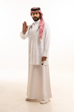 Raising hand with stop gesture, concept of medicine and healthcare, portrait of a Saudi Arabian Gulf doctor wearing traditional thobe with coat and stethoscope providing health services to patients in centers and hospitals, working in the health sector in the Kingdom, full body, white background