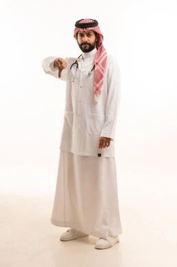  التقييم السلبي وعدم الرضى، مفهوم الطب والرعاية الصحية، بورتريه لطبيب عربي خليجي سعودي يرتدي الثوب التقليدي مع المعطف والسماعة الطبية يقدم الخدمات الصحية للمرضى ويشير باصبع الابهام للاسفل، العمل في القطاع الصحي في المملكة، الجسم بالطول الكامل، خلفيه بيضاء