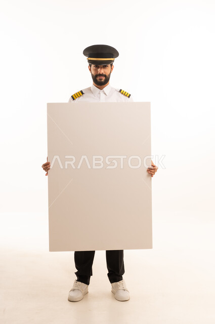 لوحات توضيحية ووسائل تعليمية، مفهوم السياحة والسفر، طاقم الاستقبال والترحيب بالركاب، العمل في مجال الطيران، رحلات جوية سياحية, خطوط الطيران السعودية, بورتريه لكابتن طيار عربي سعودي خليجي مبتسم يرتدي الزي الرسمي يحمل بيده موك اب ابيض، الجسم بالطول الكامل، خلفيه بيضاء