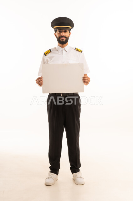 Illustrations and educational tools, the concept of tourism and travel, the reception and welcome crew, working in the aviation field, tourist flights, Saudi Airlines, a portrait of a smiling Saudi Arabian Gulf Arab pilot in uniform holding a white mock-up, full-length body, white background