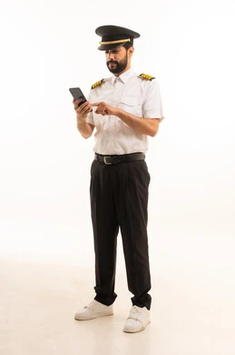 استخدام الهاتف المحمول، مفهوم السياحة والسفر، طاقم الاستقبال والترحيب بالركاب، العمل في مجال الطيران، رحلات جوية سياحية, خطوط الطيران السعودية, بورتريه لكابتن طيار عربي سعودي خليجي مبتسم يرتدي الزي الرسمي يقف باستقامة، الجسم بالطول الكامل، خلفيه بيضاء