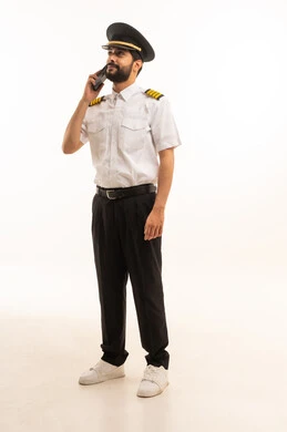 اجراء مكالمة هاتفية عبر الهاتف المحمول، طاقم الاستقبال والترحيب بالركاب، العمل في مجال الطيران، رحلات جوية سياحية,  مفهوم السياحة والسفر، خطوط الطيران السعودية, بورتريه لكابتن طيار عربي سعودي خليجي يرتدي الزي الرسمي يقف باستقامة، الجسم بالطول الكامل، خلفيه بيضاء