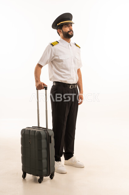 Blank black screen view on mobile phone, tourism and travel concept, welcome and reception crew, aviation work, tourist flights, Saudi Airlines, portrait of smiling Saudi Arabian Gulf Arab pilot in uniform pulling suitcase, full body, white background