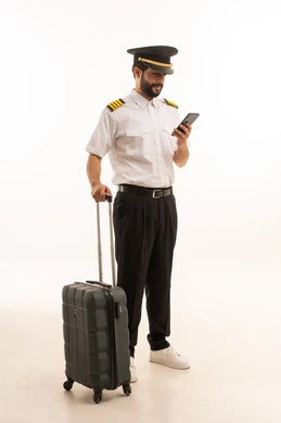 تصفح مواقع التواصل الاجتماعي عبر الهاتف المحمول، مفهوم السياحة والسفر، طاقم الاستقبال والترحيب بالركاب، العمل في مجال الطيران، رحلات جوية سياحية, خطوط الطيران السعودية, بورتريه لكابتن طيار عربي سعودي خليجي يرتدي الزي يجر الحقيبة، الجسم بالطول الكامل، خلفيه بيضاء