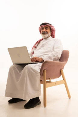 Managing and organizing business affairs through technical devices, an administrative profession and job, integrating work with technology, a portrait of a Saudi Arabian Gulf businessman wearing a traditional thobe and shemagh working on a laptop, using a modern and advanced technical device, working remotely and completing the required tasks