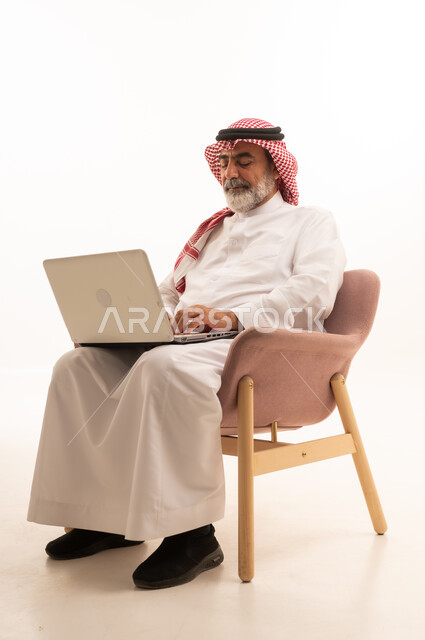 إدارة شؤون الأعمال وتنظيمها عبر الاجهزة التقنية، مهنة ووظيفة ادارية، دمج العمل مع التكنولوجيا، بورتريه لرجل عربي خليجي سعودي يرتدي الثوب التقليدي والشماغ يعمل على الحاسوب المحمول، استخدام جهاز تقني حديث ومتطور، العمل عن بعد وانجاز المهام المطلوبة، خلفية بيضاء 