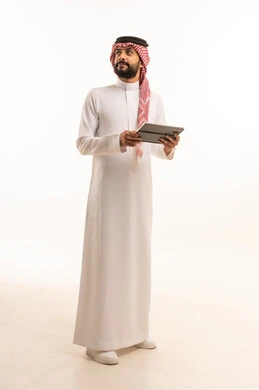 Working remotely and completing required tasks, managing and organizing business affairs through technical devices, an administrative profession and job, integrating work with technology, a portrait of a Saudi Arabian Gulf man wearing a traditional thobe and shemagh working on a tablet, using a modern and advanced technical device, a white background