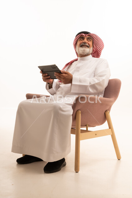 Working remotely and completing required tasks, managing and organizing business affairs through technical devices, an administrative profession and job, integrating work with technology, a portrait of a Saudi Arabian Gulf man wearing a traditional thobe and shemagh working on a tablet, using a modern and advanced technical device, a white background