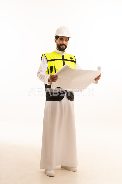 مشاريع إعمارية سعودية وطنية، مفهوم الهندسة المعمارية، متابعة مخطط المشروع الهندسي وتدقيقه, الاهتمام بالتطور العمراني بسواعد المهندسين السعوديين, بورتريه لمهندس عربي خليجي سعودي يرتدي سترة العمل وخوذة الحماية يحمل بيده المخطط، الجسم بالطول الكامل، خلفية بيضاء