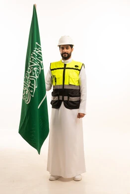 Celebrating Saudi National Day on September 23, the concept of architecture, interest in urban development by Saudi engineers, national construction projects, portrait of a Saudi Arabian Gulf engineer wearing a work jacket and a protective helmet standing next to the Kingdom's flag, full-length body, white background