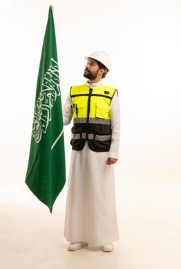 الاحتفال بذكرى اليوم الوطني السعودي 23 سبتمبر، مفهوم الهندسة المعمارية، الاهتمام بالتطور العمراني بسواعد المهندسين السعوديين، مشاريع إعمارية وطنية، بورتريه لمهندس عربي خليجي سعودي يرتدي سترة العمل وخوذة الحماية يقف بجانب علم المملكة، الجسم بالطول الكامل، خلفية بيضاء