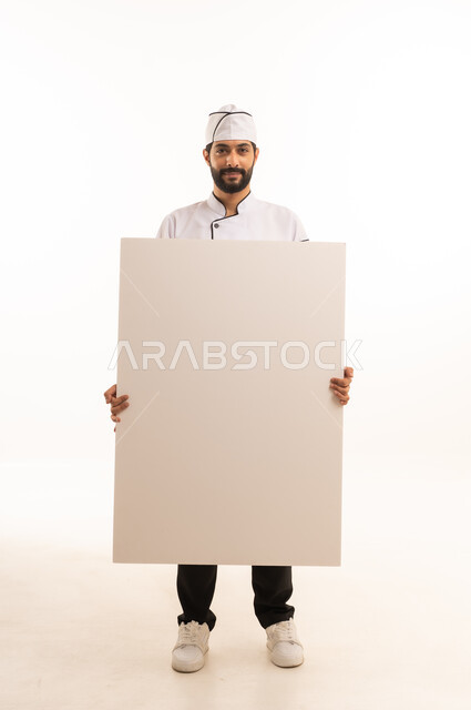 موك اب ابيض كبير, احتراف مهنة طهي الطعام السعودي, الوقوف باستقامة وتعابير السعادة, بورتريه لشيف عربي خليجي سعودي يرتدي يونيفورم الطبخ يمسك بيده لوحة بيضاء فارغة، الجسم بالطول الكامل, خلفية بيضاء