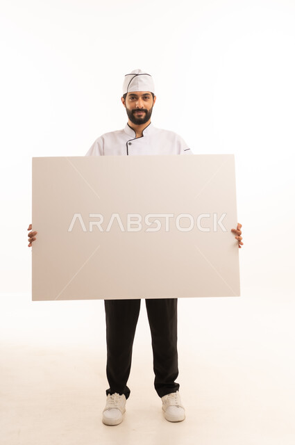 موك اب ابيض كبير, احتراف مهنة طهي الطعام السعودي, الوقوف باستقامة وتعابير السعادة, بورتريه لشيف عربي خليجي سعودي يرتدي يونيفورم الطبخ يمسك بيده لوحة بيضاء فارغة، الجسم بالطول الكامل, خلفية بيضاء