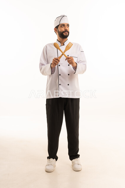 احتراف مهنة طهي الطعام السعودي, الوقوف باستقامة وتعابير السعادة, بورتريه لشيف عربي خليجي سعودي يرتدي يونيفورم الطبخ يمسك بيده ادوات خشبية بايماءات السرور، الجسم بالطول الكامل, خلفية بيضاء