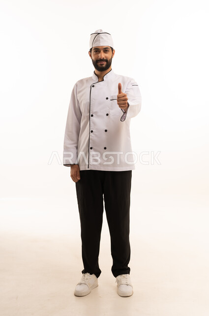 احتراف مهنة طهي الطعام السعودي, رفع اصبع الابهام لاعلى بتعابير القبول والرضا, بورتريه لشيف عربي خليجي سعودي يرتدي يونيفورم الطبخ ينظر إلى الكاميرا بايماءات الاعجاب والفخر، الجسم بالطول الكامل, خلفية بيضاء