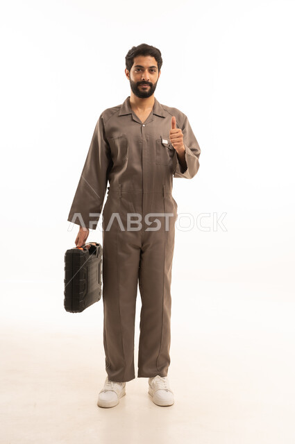 Thumbs up expression of quality and admiration, skill and workmanship, use of maintenance equipment to make repairs, portrait of a Saudi Arabian Gulf man wearing work uniform holding a tool bag, full body, white background