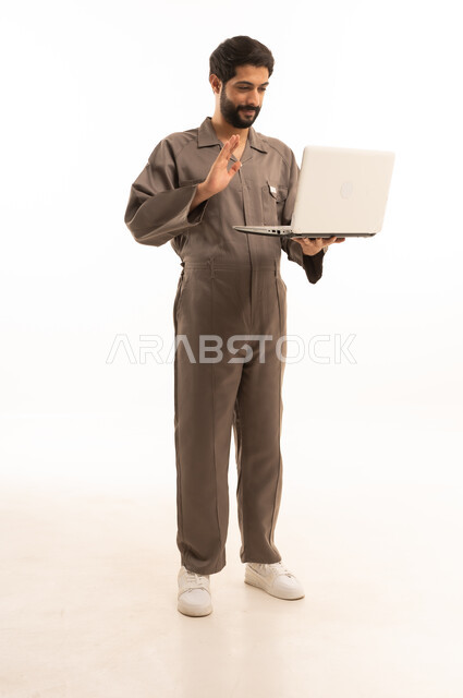 Using modern technical equipment, skill and mastery of work, using maintenance equipment to make repairs, portrait of a Saudi Arabian Gulf man wearing a work uniform holding a laptop, full body, white background