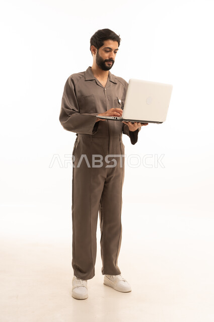 Using modern technical equipment, skill and mastery of work, using maintenance equipment to make repairs, portrait of a Saudi Arabian Gulf man wearing a work uniform holding a laptop, full body, white background