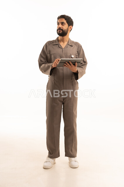 استخدام جهاز تقني حديث, المهارة و اتقان العمل، استعمال معدات الصيانة لاجراء التصليحات، بورتريه لرجل عربي سعودي خليجي يرتدي يونيفورم العمل يحمل جهاز التابلت اللوحي, الجسم بالطول الكامل، خلفية بيضاء