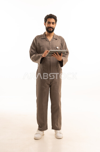 Using modern technical equipment, skill and mastery of work, using maintenance equipment to make repairs, portrait of a Saudi Arabian Gulf man wearing work uniform holding a tablet, full body, white background
