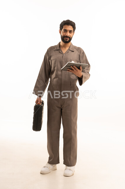 استخدام جهاز تقني حديث, المهارة و اتقان العمل، استعمال معدات الصيانة لاجراء التصليحات، بورتريه لرجل عربي سعودي خليجي يرتدي يونيفورم العمل يحمل بيده حقيبة الادوات وجهاز التابلت اللوحي, الجسم بالطول الكامل، خلفية بيضاء