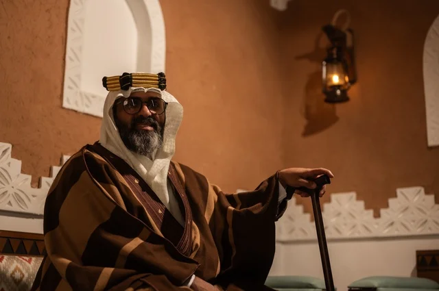 صورة جانبية لرجل عربي سعودي مسن يرتدي الزي العربي التقليدي يجلس على كرسي خشبي داخل غرفة تراثية بديكورات جدران مزخرفة، يرتدي عباءة واسعة وعقالًا على رأسه، ويبدو بلحية بيضاء، بيده عكاز يستند إليها، الحكمة والتجربة الطويلة في الحياة. صورة جانبية لرجل عربي سعودي مسن يرتدي الزي العربي التقليدي يجلس على كرسي خشبي داخل غرفة تراثية بديكورات جدران مزخرفة، يرتدي عباءة واسعة وعقالًا على رأسه، ويبدو بلحية بيضاء، بيده عكاز يستند إليها، الحكمة والتجربة الطويلة في الحياة.