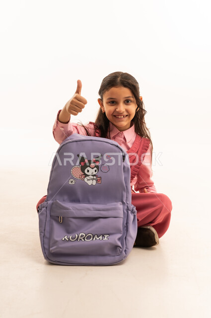  الاستعداد للعام الدراسي الجديد,  تعابير وإيماءات السعادة و السرور, بورتريه لفتاة عربية خليجية سعودية مبتسمه ترتدي الزي المدرسي تقوم بتوضيب حقيبتها المدرسية، التجهز للذهاب الى اليوم الاول في المدرسة، حب التعلم و التعليم, خلفية بيضاء