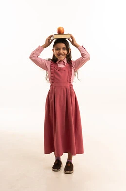 Eating healthy fruits, preparing for the new school year, loving learning and education, looking at the camera with gestures of happiness and pleasure, portrait of a Saudi Arabian Gulf girl wearing a school uniform with school books and a green apple on her head, full body, white background